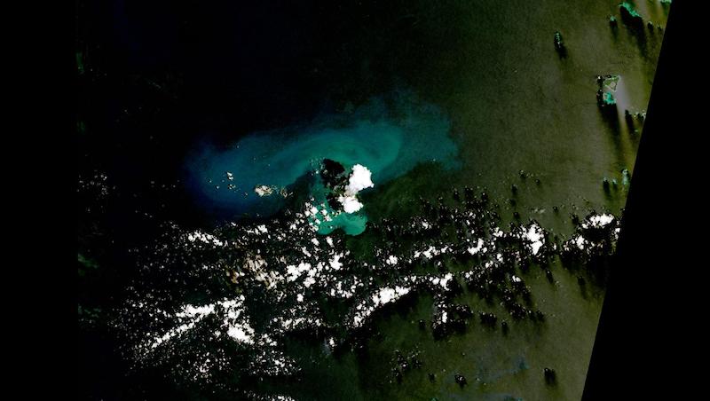 Image of white volcanic plume over bluish/black ocean