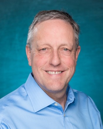 A headshot of Dr. Frederick Bingham, Professor, University of North Carolina Wilmington, Department of Physics & Physical Oceanography who uses NASA Earth science data to study ocean dynamics. In this image, Bingham is a middle-aged man with short gray hair. He's wearing a blue oxford shirt and posing before a turquoise bachground.