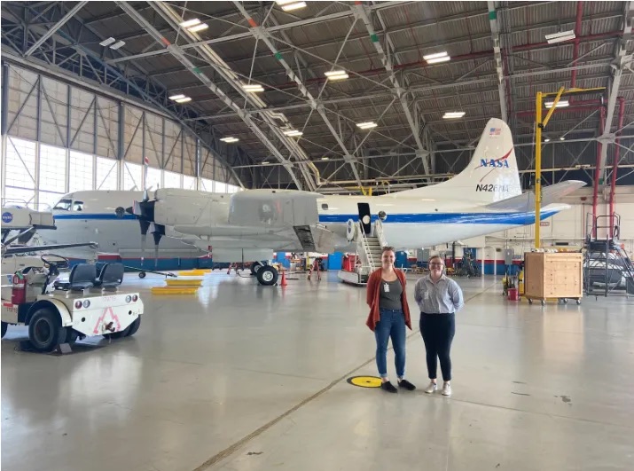 Shelby Bagwell and Ashlyn Shirey stand in front of a P-3 aircraft in a hanger