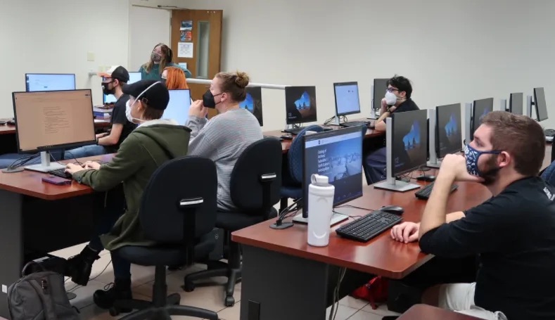 College students sit in a lecture hall in front of computer screens