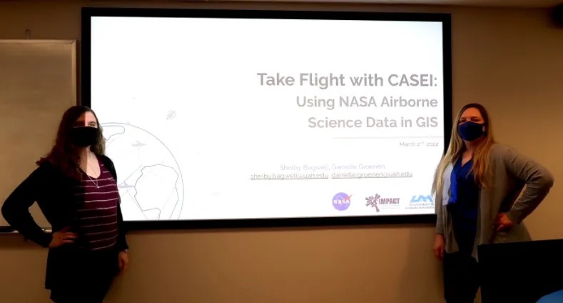 Shelby Bagwell and Dr. Danielle Groenen, both wearing masks, stand before a screen that reads "“Take Flight with CASEI: Using NASA Airborne Science Data in GIS.”
