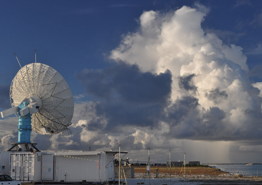 A weather radar sits on a shipping container on Addu Atoll in the Indian Ocean where the Madden-Julian Oscillation spawns. Convective clouds form in the background. (Courtesy E. Maloney/Colorado State University)