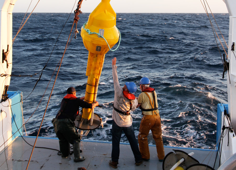 Photograph of a crew hauling an ocean buoy onboard a ship
