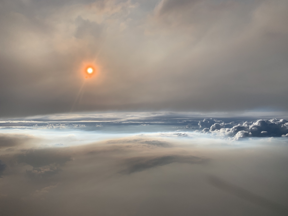 Peterson captured this image of the setting Sun shining through thick smoke at 8 p.m. Mountain Time while flying aboard a NASA DC-8 at an altitude of roughly 30,000 feet (9 kilometers). Particles in the smoke reflect light in ways that make the Sun appear orange. The photograph below shows the smoke plume (gray) that fed the pyrocumulonimbus cloud (white). 