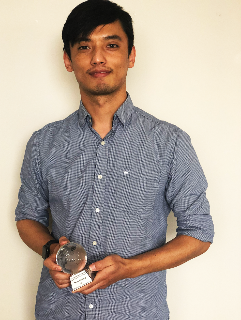 Iksha Gurung holds his UAH Earth Systems Science Center (ESSC) 2022 Meritorious Service Award, which is shaped like a small, clear globe.