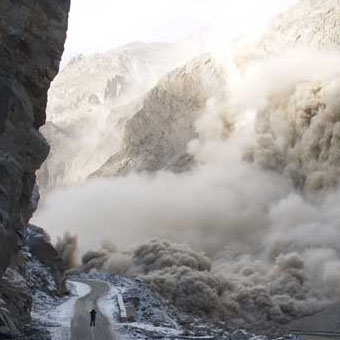 A man stands in the middle of the Karakoram Highway while rocks tumble down into the Hunza River in Pakistan’s Gojal region.
