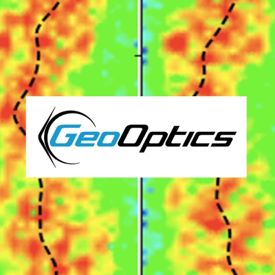 This is a combined image comprised of the GeoOptics company logo layered on top of an image showing measurements of GPS radio signals passing through the atmosphere. The "Geo" portion of the logo is blue while "Optics" is black. The logo is inside a white rectangle. The satellite imagery has a green background covered with blotches of red, orange, and yellow. The red blotches mark areas of the atmosphere where GPS signals passed through on their way to a GeoOptics satellite trying to receive them on the oth