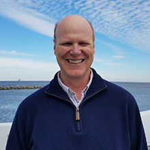 lehrter standing in front of a body of water on a sunny day wearing a blue pullover
