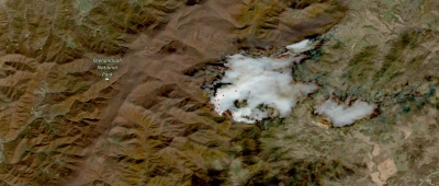 Clear sky image of brown mountains with white smoke in the center; red dots indicating hotspots are on the left side of the center smoke