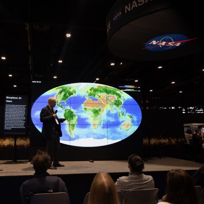 NASA researcher stands in front of the Hyperwall displaying a map of Earth