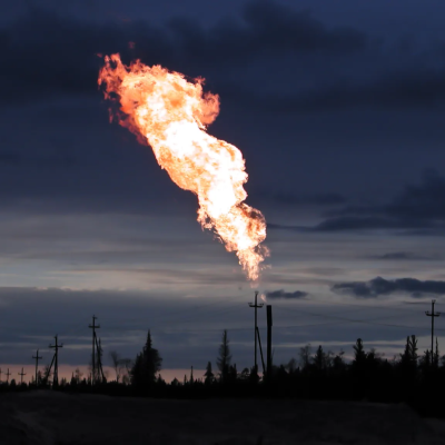 Outdoor evening image of a fiery methane plume coming out of a tall black pipe. 