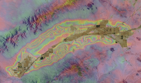 Interferogram with bands of colors indicating changes in land elevation. Center of image has brown strip indicating roads and infrastructure of McMullen, AZ.