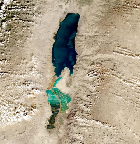 Body of water in the desert in center of image; green salt pans to south