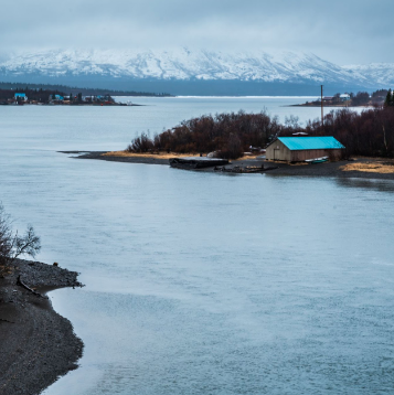 Image of river with snow-capped mountains in background; small settlement on right side of river