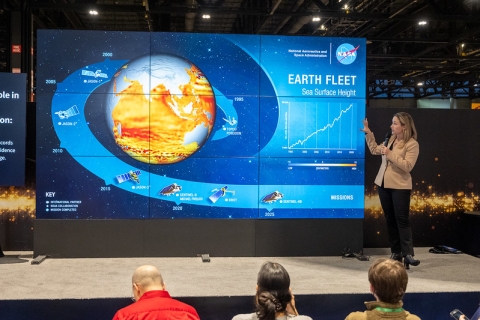 woman standing at right side of NASA Hyperwall with image of Earth and sea level rise on screen