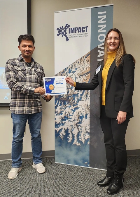 Cerese Albers presents Anish Bhusal with an IMPACT Award while standing in front of an IMPACT Innovate banner