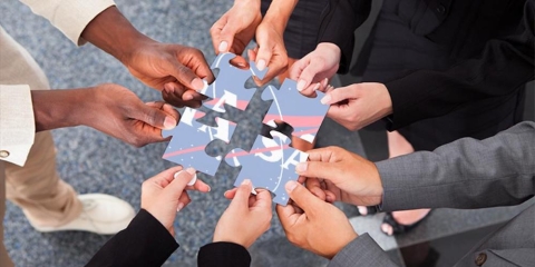 Four people each hold a puzzle piece, together which forms the NASA logo
