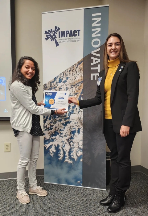 Cerese Albers presents Slesa Adhikari with an IMPACT Award while standing in front of an IMPACT Innovate banner