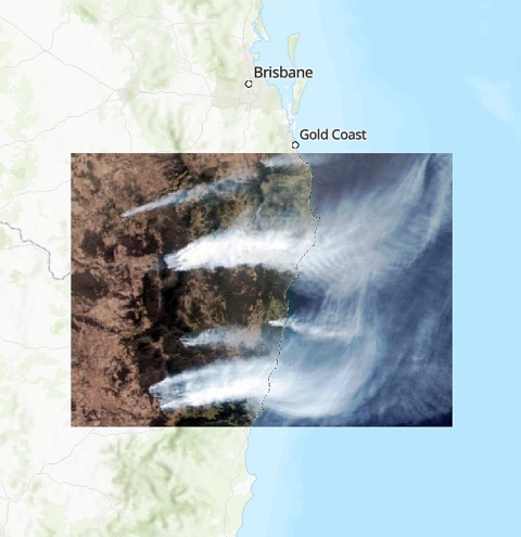 This two-layer image shows an image of bushfires in Eastern Australia in 2019. The top of layer of the image shows a true color scan of the area from the Suomi NPP satellite. On the left is brown and green land with smoke plumes streaming to the right and East out across the ocean. The bottom layer of the image is an illustrated map showing the same area and labeling the Brisbane and Gold Coast communities.