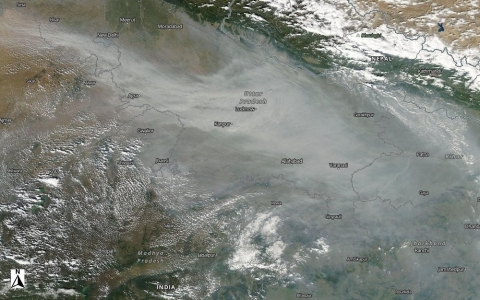 NASA Worldview image of India showing a milky-white cloud of aerosols from agricultural burning extending from the southeast to the northwest; bright white clouds are seen to the south and north of the milky white aerosols. Indian city names are overlain on the image, with New Delhi near the center.
