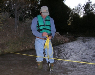 Thoma standing in a stream and taking a measurement.