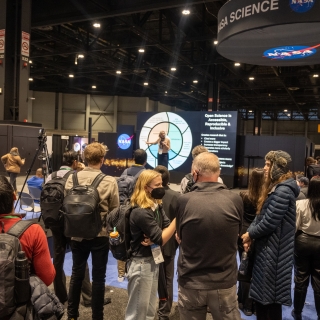 A crowd watches a NASA scientist present in front of the Hyperwall