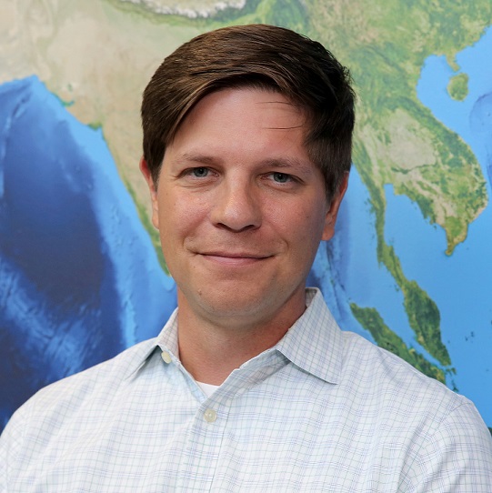 Headshot of Kevin Murphy standing in front of a world map.