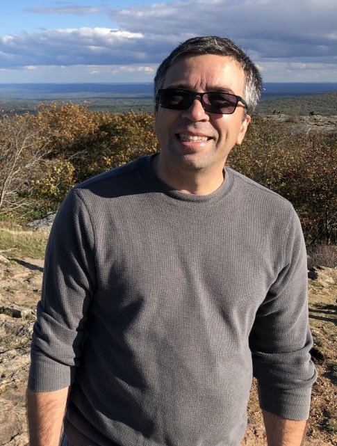 Image of Dr. Paul Siqueira standing on a mountain wearing a light sweater and sunglasses.