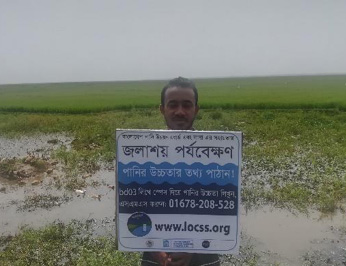 Man holding sign written in Bangla explaining the Citizen Science lake project.