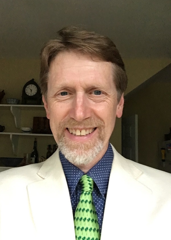 Indoor headshot of Dr. Chris Lynnes wearing a white suit with a green necktie.